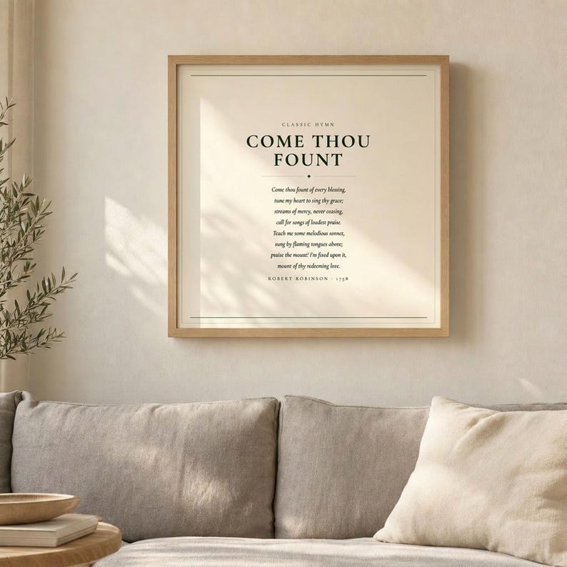 Come Thou Fount of Every Blessing hymn lyric wall art print above grey linen sofa in bright airy living room with olive branch, light oak wood frame, natural window light and palm leaf shadows, christian minimalist home decor, come thou fount art print song lyric baptism confirmation first communion gift