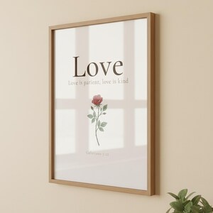 Love Fruit of the Spirit Christian wall art print featuring Galatians 5:22, with beautiful red rose botanical illustration, in minimalist botanical watercolor illustration on warm cream background with elegant serif typography, displayed in a bright modern entryway next to a coat rack with natural greenery, serving as welcoming faith-filled home decor