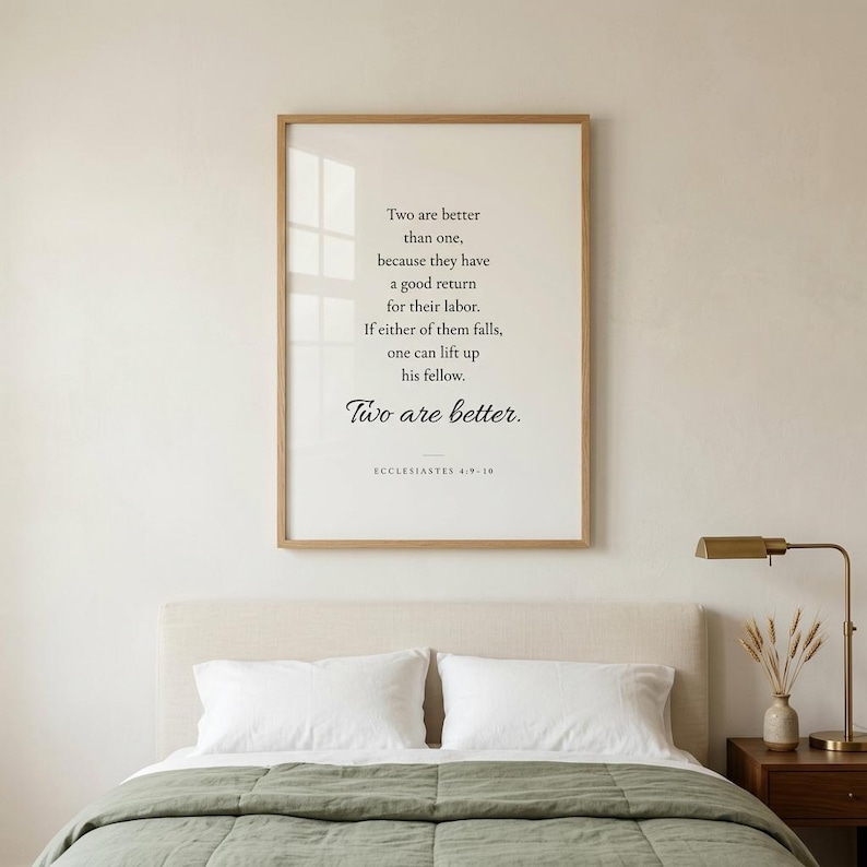 Ecclesiastes 4:9-10 'Two Are Better Than One' Christian wedding wall art in modern minimalist serif typography on cream, framed in natural oak in a romantic newlywed living room with white peonies and eucalyptus. Premium Christian wedding digital download, newlywed gift, first anniversary keepsake, bridal shower.