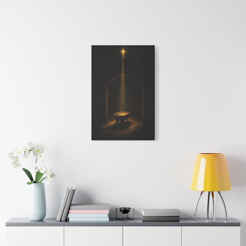 Styled Christmas living room preview: Dark vintage oil painting on canvas showing the Star of Bethlehem shining above an empty wooden manger inside a rustic stable. A warm golden beam falls across rough timber, straw, and the humble crib, creating a reverent nighttime scene. Matthew 2:2 nativity wall art in deep brown and gold tones, printed on stretched canvas and ready to hang.