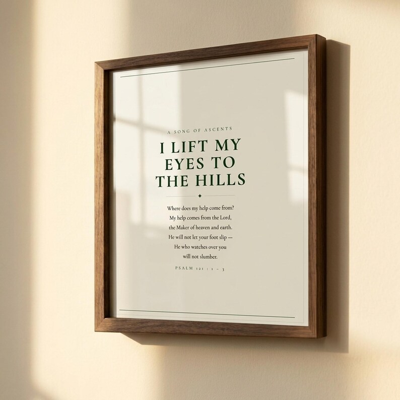 Close-up detail of Psalm 121 I Lift My Eyes to the Hills scripture print in warm walnut float frame with glass and natural golden window light casting soft shadows, dark forest green Cormorant Garamond serif typography on warm cream paper, christian wall art close-up lift my eyes psalm 121 print housewarming baptism gift