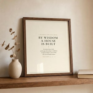 Proverbs 24:3 By Wisdom A House Is Built scripture print leaning on wooden shelf with dried botanical and round ceramic vase beside a journal, walnut frame with glass, warm cream neutral tones, christian home decor wall art housewarming gift, house blessing scripture print for entryway bedroom living room new home