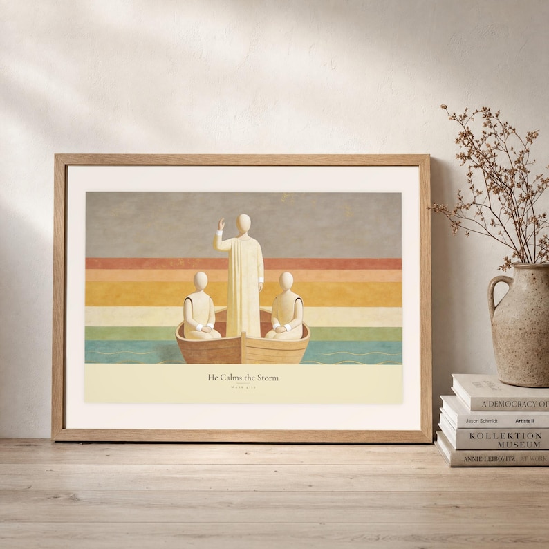 Leaning frame mockup of He Calms the Storm on a rustic wood console beside stacked art books and a tall ceramic vessel with dried stems. The print shows Christ standing in a wooden boat with a raised hand above calm layered water. The oak frame, broad cream mat, plaster wall, and soft side light create a relaxed display while keeping the title and Mark 4:39 legible.