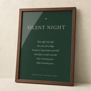 Close frontal view of a Silent Night Christmas print in a rich walnut frame, cropped to emphasize the artwork. Deep forest green surrounds cream serif typography, a small gold star ornament, the centered first verse, and Traditional Christmas Hymn footer. This minimalist holiday print offers classic Christmas hymn wall art for tasteful Christian Christmas decor.
