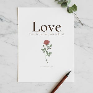 Love Fruit of the Spirit Christian wall art print featuring Galatians 5:22, with beautiful red rose botanical illustration, in minimalist botanical watercolor illustration on warm cream background with elegant serif typography, presented as an elegant flat lay on white marble with a fountain pen and eucalyptus sprig, showing the complete print design in full detail
