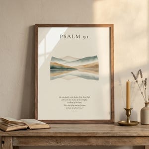 Custom scripture print framed in rustic walnut hardwood with clear glass front showing diagonal reflection, leaning on a weathered oak console next to an open vintage leather book, brass candlestick with beeswax candle, and small ceramic vase with dried lavender, warm golden-hour light, cottage editorial Christian home decor digital download