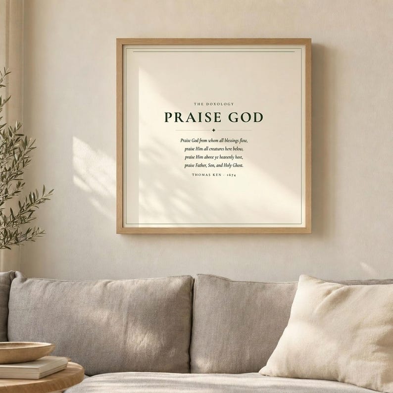 Doxology Praise God From Whom All Blessings Flow hymn lyric wall art print above grey linen sofa in bright airy living room with olive branch, light oak wood frame, natural window light and palm shadows, christian minimalist home decor, doxology print song lyric art baptism confirmation wedding gift