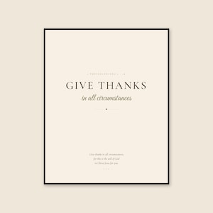 Framed 1 Thessalonians 5:18 Scripture print on a warm cream background, featuring dark brown display serif text reading GIVE THANKS and olive script reading in all circumstances. The calm, earthy design presents a clear message of gratitude and faith for a living room, entryway, bedroom, office, prayer corner, or understated autumn display.