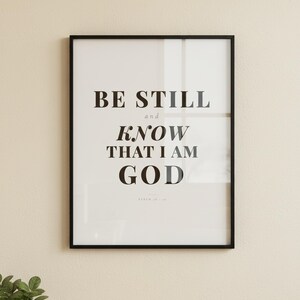 Psalm 46 10 Wall Art Be Still and Know That I Am God Scripture Print Christian, in contemporary bold serif typography in black on clean white background, displayed in a bright modern entryway next to a coat rack with natural greenery, serving as welcoming faith-filled home decor. Instant digital download printable wall art in multiple sizes for easy home printing