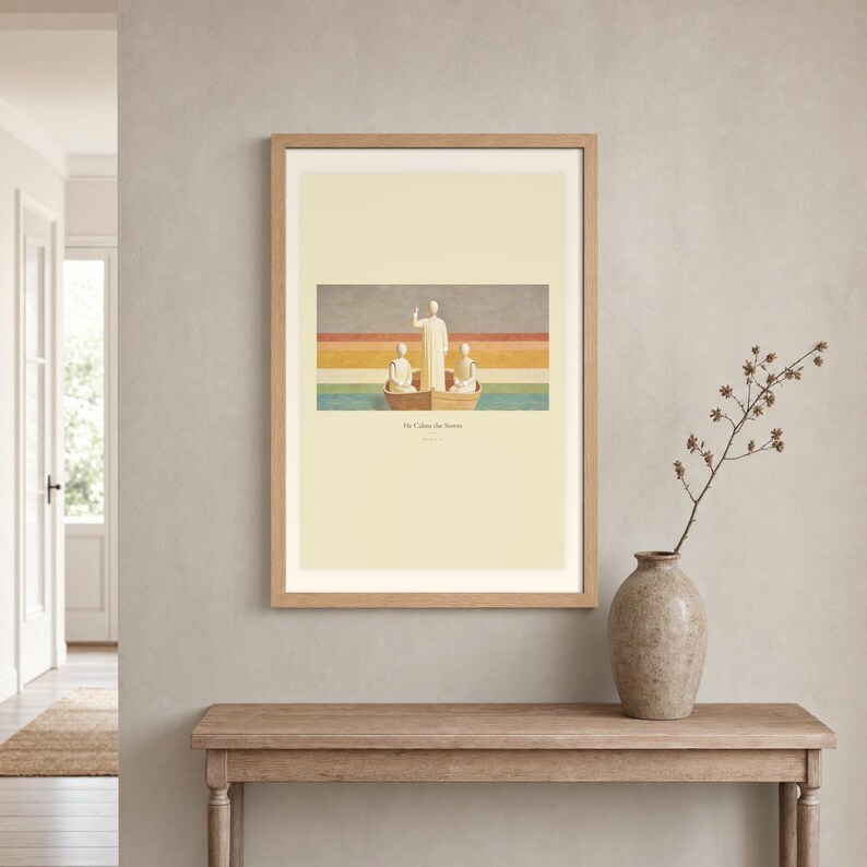 Room mockup of He Calms the Storm displayed in a light oak frame on a warm neutral wall. The landscape artwork shows Christ standing in a wooden boat with a raised hand above calm layered water. A wide cream mat and restrained fresco palette suit a calm living room, prayer space, or Christian home. The printed title and Mark 4:39 remain visible beneath the image.