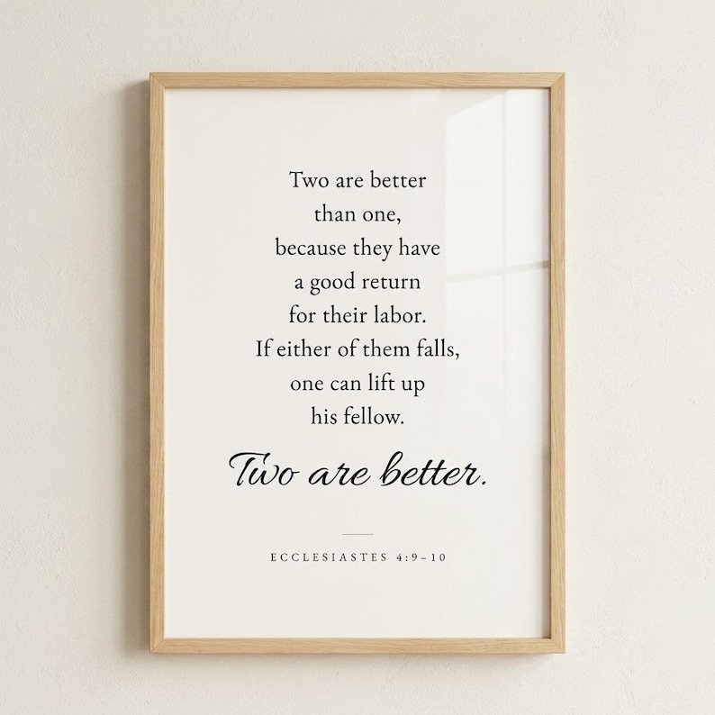 Studio hero shot of Ecclesiastes 4:9-10 'Two Are Better Than One' wedding scripture print in natural oak wood frame on warm off-white plaster wall, subtle glass reflection. Modern minimalist Christian wedding wall art, instant download, perfect newlywed gift, first anniversary, wedding gift print.