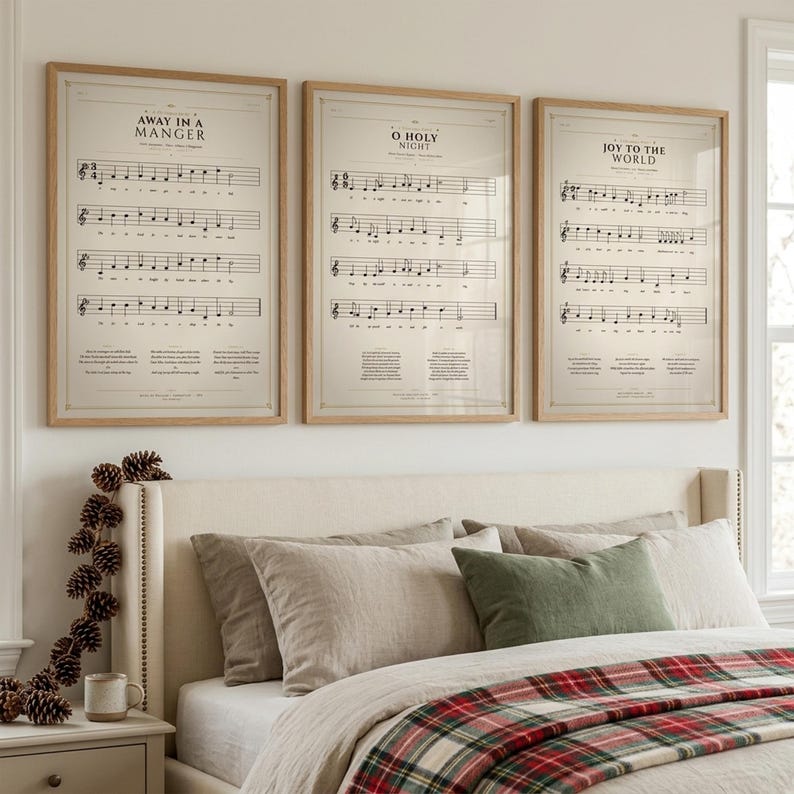 Christmas hymns gallery wall set — Away in a Manger, O Holy Night, Joy to the World — three vintage hymnal prints in oak frames above cream bed with tartan throw and linen pillows, pinecone garland on nightstand, soft Christmas morning light, holiday bedroom christian wall art download TheFramedVerse Etsy