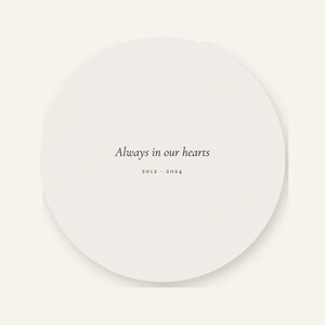 Clean back artwork view of the personalized acrylic pet memorial ornament, showing the words Always in our hearts centered on the round keepsake. Soft watercolor details coordinate with the front while the ribbon opening and smooth circular edge remain visible. The plain background clearly presents the double sided printing included with this physical remembrance ornament.