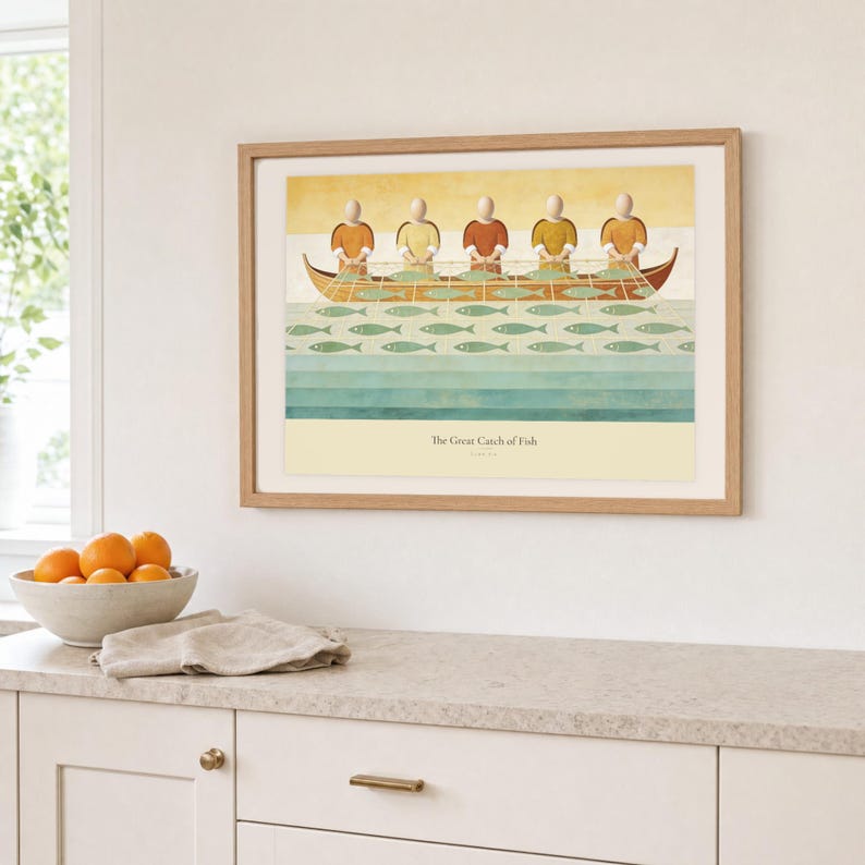 Kitchen mockup of The Great Catch of Fish framed in light oak above a pale stone counter, white cabinetry, a linen cloth, and a bowl of oranges. The artwork shows faceless fishers lifting a broad net filled with sage fish beside a wooden boat. Bright window light and the warm cream mat demonstrate how the Christian print works in a clean, welcoming kitchen interior.