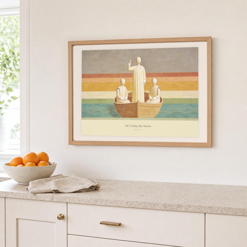 Kitchen mockup of He Calms the Storm framed in light oak above a pale stone counter, white cabinetry, a linen cloth, and a bowl of oranges. The artwork shows Christ standing in a wooden boat with a raised hand above calm layered water. Bright window light and the warm cream mat demonstrate how the Christian print works in a clean, welcoming kitchen interior.