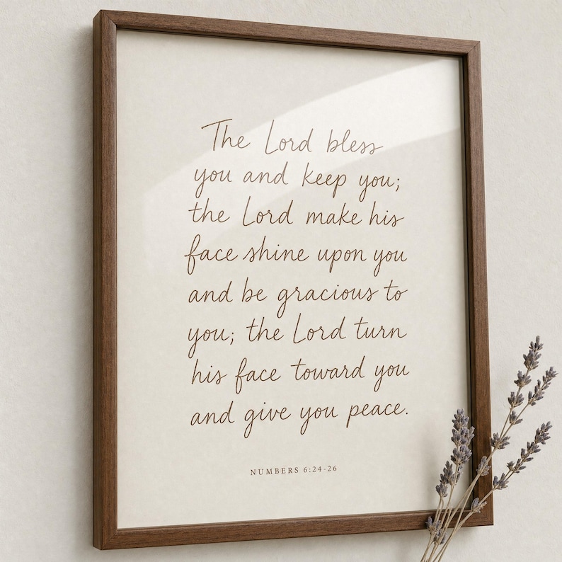 Premium close-up of the Numbers 6:24-26 hand-lettered priestly blessing in a warm oak frame, slightly angled with a soft sprig of dried wildflowers in the foreground bokeh and clear glass reflection. Aaronic blessing 'The Lord bless you' Christian wedding bible verse wall art, instant digital download.