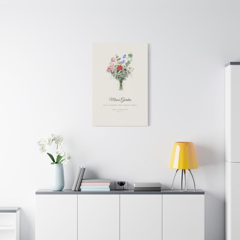 Printify room context showing a personalized Birth Flower Family Bouquet Canvas above a neutral sofa. The 16x20 inch stretched canvas combines watercolor birth month flowers, family names and the title Mom's Garden in a warm botanical arrangement. This ready to hang family canvas art is shown at home as a Christmas gift for mom or grandma, Mother's Day present or housewarming keepsake.