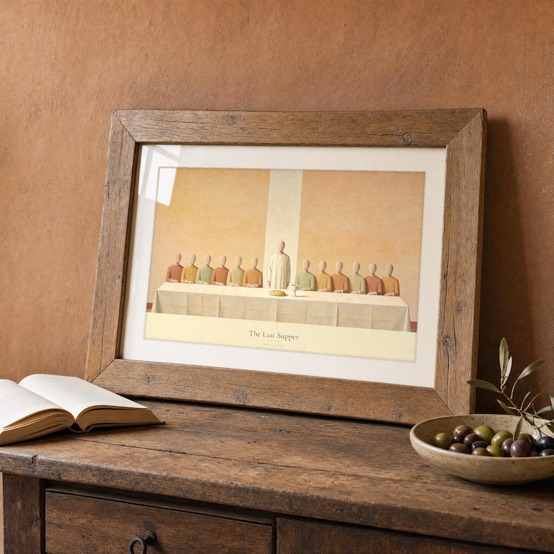 The Last Supper print in a rustic walnut landscape frame leaning on a weathered oak console beside an open leather Bible, a brass candlestick and a small stoneware jug with dried wheat. Warm golden hour light rakes across the plaster wall behind it, terracotta and olive earth tones throughout. Luke 22:19 Christian home decor digital download from TheFramedVerse on Etsy.