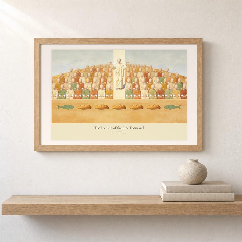 Shelf mockup of The Feeding of the Five Thousand in a light oak frame resting on a pale wood surface beside stacked neutral books and a rounded ceramic vase. The framed print shows Christ raised on the centre axis above a seated hillside crowd, with loaves and fish laid out along the foreground. Cream matting, soft wall texture, and natural light present the horizontal Bible artwork at an easy domestic scale.