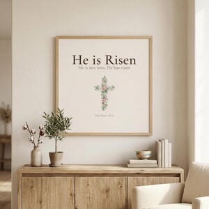 Easter He is Risen Scripture Art Set, Floral Cross Bible Verse Prints, — "He is not here; He has risen, just as He said", in beautiful floral cross composed of spring roses, greenery and wildflowers, showcased in an elegant contemporary home interior with curated decor elements, demonstrating how this Christian art piece elevates any living space