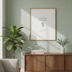 Consider the Lilies Matthew 6:28 sage green botanical scripture print above light grey linen sofa with cream throw pillows and terracotta planter, minimalist christian living room gallery wall, floral scripture digital download scriptural wall art from TheFramedVerse Etsy shop baptism gift
