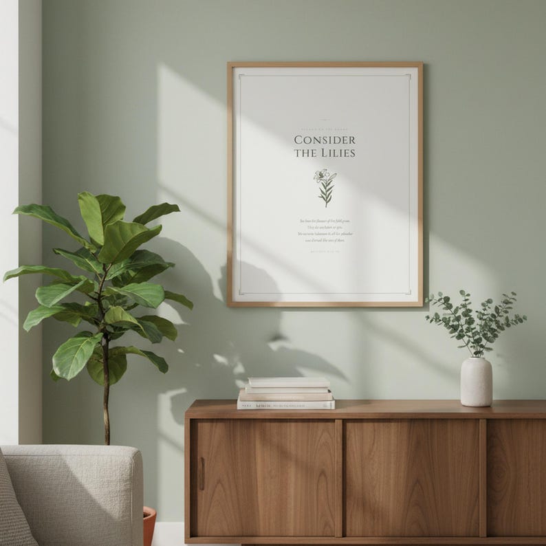 Consider the Lilies Matthew 6:28 sage green botanical scripture print above light grey linen sofa with cream throw pillows and terracotta planter, minimalist christian living room gallery wall, floral scripture digital download scriptural wall art from TheFramedVerse Etsy shop baptism gift