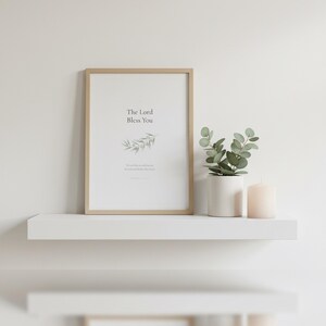 The Lord Bless You Numbers 6 24 26 Nursery Bible Verse Print Christian Wall Art, — "The Lord bless you and keep you; the Lord make His face shine on you", in gentle sage green nursery design with soft botanical watercolor illustration and calming earth tones, photographed in beautiful close-up detail showing the premium glass frame reflection, the crisp typography and the intricate artistic