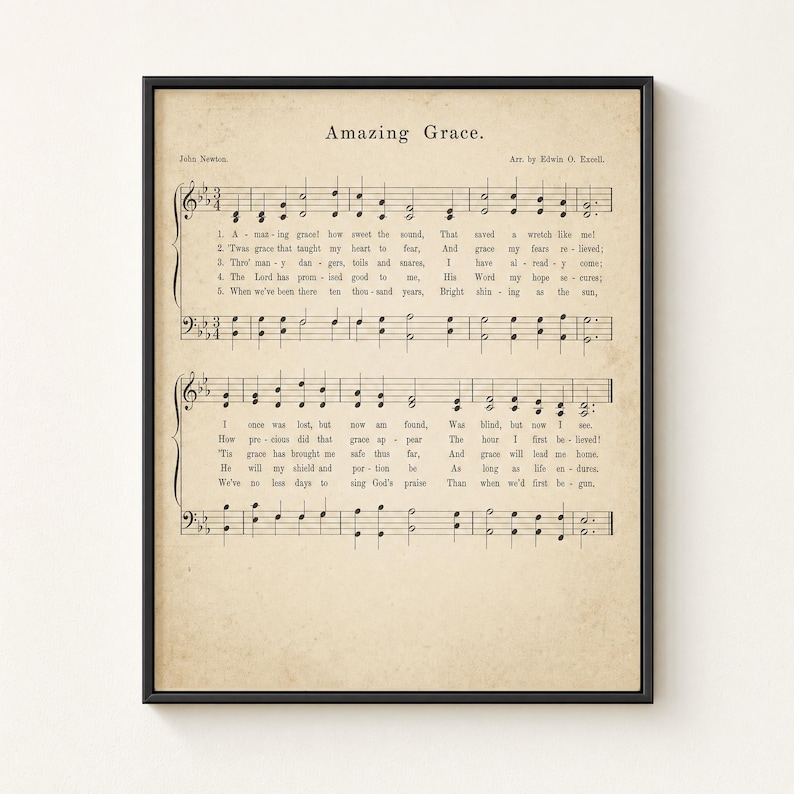 Amazing Grace vintage sheet music wall art framed frontal in a slim matte black metal frame on a warm cream limewashed plaster wall. Aged hymnal page with John Newton 1779 hymn notation, perfect Christian farmhouse home decor, instant digital download from TheFramedVerse on Etsy.