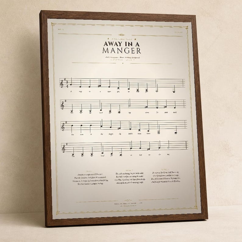 Away in a Manger vintage sheet music print in a solid walnut frame, frontal studio shot on a cream backdrop with soft top-left key light and gentle glass reflection. Classical Christmas hymn wall art digital download from TheFramedVerse — single hymnal page reproduction of Luke 2:7 in warm sepia, cream, and soft black tones.