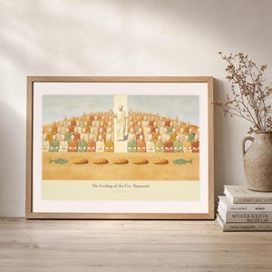 Leaning frame mockup of The Feeding of the Five Thousand on a rustic wood console beside stacked art books and a tall ceramic vessel with dried stems. The print shows Christ raised on the centre axis above a seated hillside crowd, with loaves and fish laid out along the foreground. The oak frame, broad cream mat, plaster wall, and soft side light create a relaxed display while keeping the title and Matthew 14:21 legible.