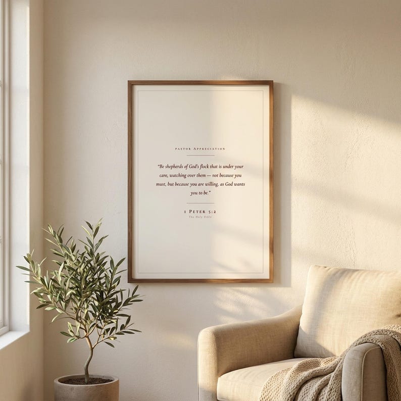 Pastor appreciation Christian wall art print featuring 1 Peter 5:2 Be shepherds of God's flock in elegant serif typography on cream paper. Framed in walnut wood above a beige armchair beside an olive tree in warm light. Minimalist scripture decor and thank you gift for a pastor, minister or church leader. Instant digital download printable.