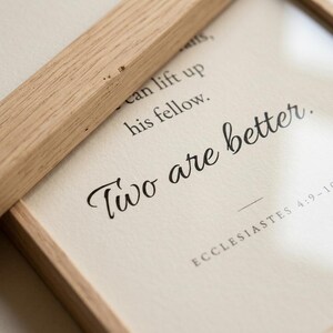 Close-up macro detail of Ecclesiastes 4:9-10 'Two are better.' in elegant Allura cursive script on premium matte fine-art paper, natural oak frame edge visible. Modern minimalist Christian wedding typography wall art, instant digital download, newlywed gift, first anniversary, engagement print.