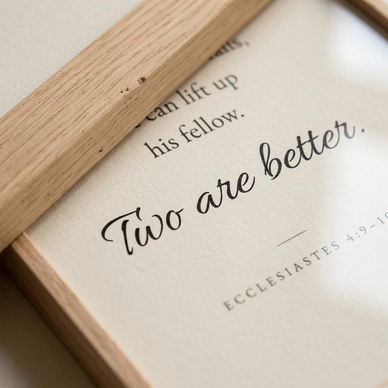 Close-up macro detail of Ecclesiastes 4:9-10 'Two are better.' in elegant Allura cursive script on premium matte fine-art paper, natural oak frame edge visible. Modern minimalist Christian wedding typography wall art, instant digital download, newlywed gift, first anniversary, engagement print.
