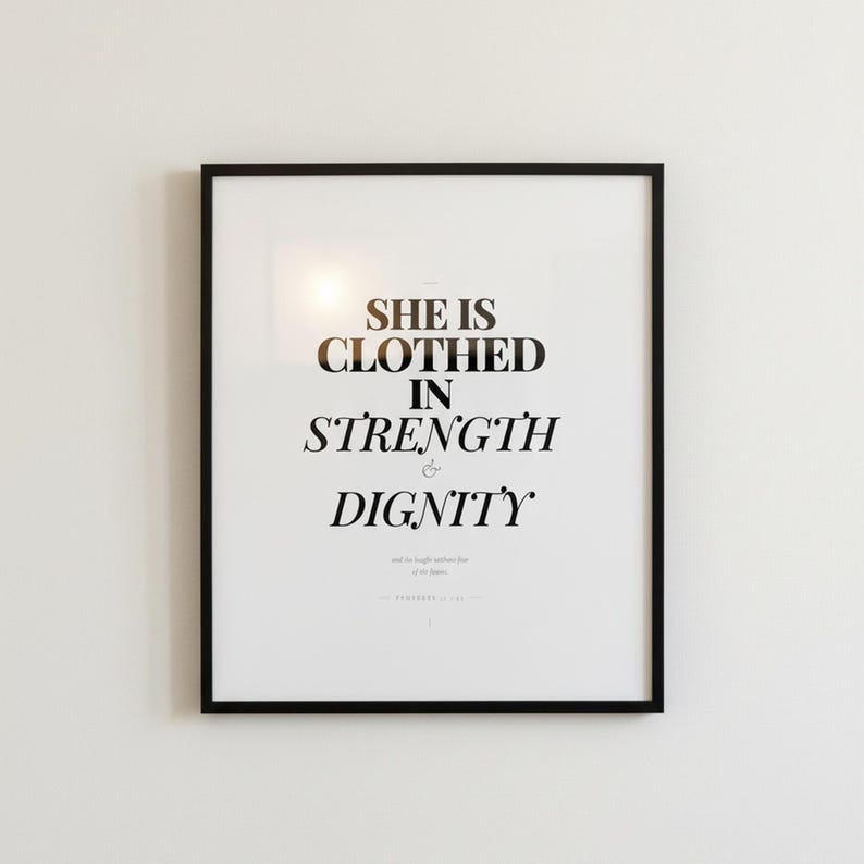 Proverbs 31 25 Wall Art She is Clothed in Strength and Dignity Scripture Print, in elegant Mother's Day design with soft pink watercolor botanical flowers and graceful serif typography, styled on a wooden floating shelf next to a ceramic vase with dried eucalyptus, creating a warm and inviting Christian home decor vignette