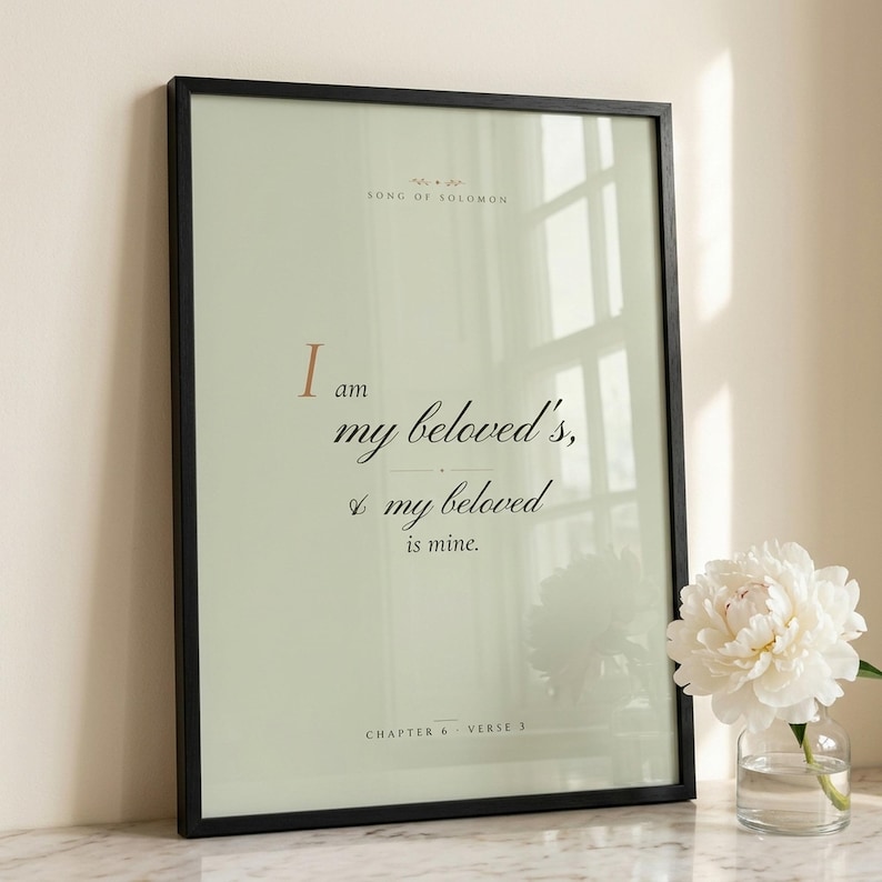 Song of Solomon 6:3 'I Am My Beloved's' coquette sage Christian wedding scripture print in thin black wood frame on white Carrara marble, single sage olive branch and white peony casting soft shadow, two unlit votive candles, warm beige textured wall, bright morning light with clean glass reflection, editorial bridal still life print download from TheFramedVerse