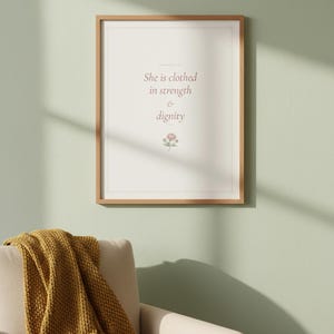 She Is Clothed in Strength and Dignity Proverbs 31 25 Wall Art Coquette Christia — front facing framed mockup on clean white wall with shadow. This coquette bow, botanical, pink blush christian scripture wall art print features beautiful serif typography on warm cream background. Proverbs 31 25 bible verse digital download printable for home office bedroom living room gallery wall decor. Perfec...