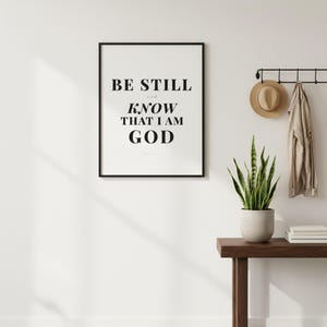 Psalm 46 10 Wall Art Be Still and Know That I Am God Scripture Print Christian, in contemporary bold serif typography in black on clean white background, styled on a wooden floating shelf next to a ceramic vase with dried eucalyptus, creating a warm and inviting Christian home decor vignette