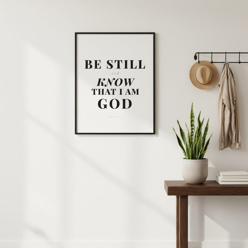 Psalm 46 10 Wall Art Be Still and Know That I Am God Scripture Print Christian, in contemporary bold serif typography in black on clean white background, styled on a wooden floating shelf next to a ceramic vase with dried eucalyptus, creating a warm and inviting Christian home decor vignette