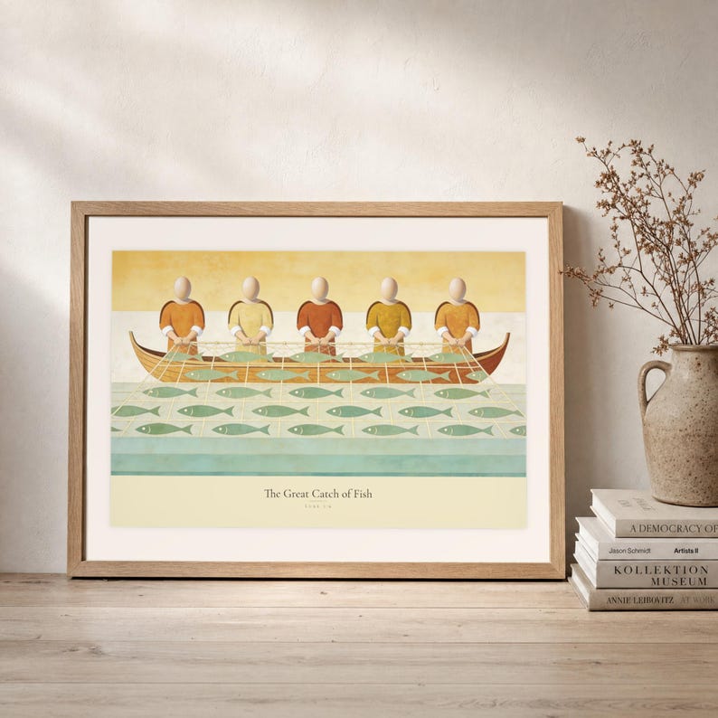Leaning frame mockup of The Great Catch of Fish on a rustic wood console beside stacked art books and a tall ceramic vessel with dried stems. The print shows faceless fishers lifting a broad net filled with sage fish beside a wooden boat. The oak frame, broad cream mat, plaster wall, and soft side light create a relaxed display while keeping the title and Luke 5:6 legible.