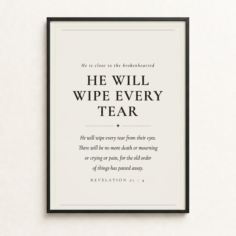 Styled shelf scene with the framed design beside an open Bible, natural botanicals, ceramics, and warm ambient light. The He Will Wipe Every Tear artwork presents Revelation 21:4 in minimalist black typography on warm beige. This Revelation 21:4 print suits a sympathy gift, memorial space, prayer room, bedroom, or comforting Christian home as printable digital wall art.