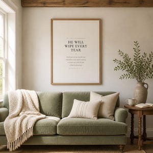 Botanical glass frame scene with the artwork near leafy stems, gentle reflections, warm wood, and soft natural light. The He Will Wipe Every Tear artwork presents Revelation 21:4 in minimalist black typography on warm beige. This Revelation 21:4 print suits a sympathy gift, memorial space, prayer room, bedroom, or comforting Christian home as printable digital wall art.