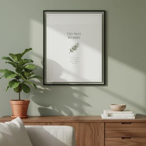 Do Not Worry Matthew 6 scripture wall art in thin black frame on white marble surface beside fresh eucalyptus stem and unlit votive candles, bright morning window light, clean glass reflection visible, floral scripture elegant bible print godly wall art digital download by TheFramedVerse Etsy