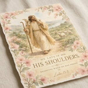 Close-up studio detail of He Lays It On His Shoulders Luke 15:5 watercolor print showing soft brushstroke texture, cherry blossom border, Jesus carrying lamb on his shoulders, and elegant Scripture typography. Premium watercolor christian wall art digital download — baptism gift, christian nursery, parable lost sheep print.