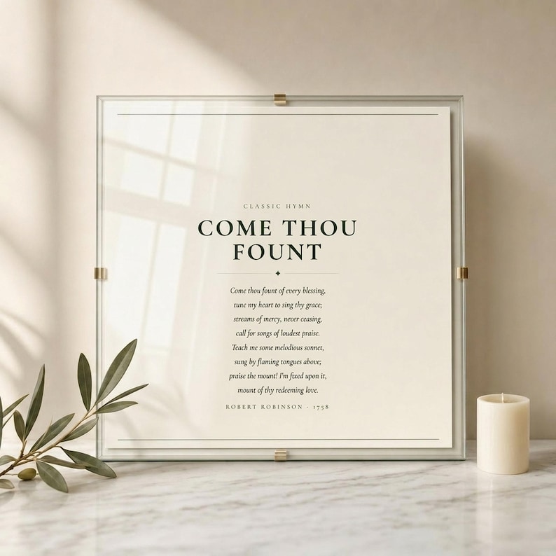 Come Thou Fount of Every Blessing hymn lyric print in floating glass frame with brass corner clips on marble surface with fresh olive branch and cream candle, dark forest green on warm cream, premium christian hymn wall art, come thou fount art song lyric art baptism confirmation first communion gift
