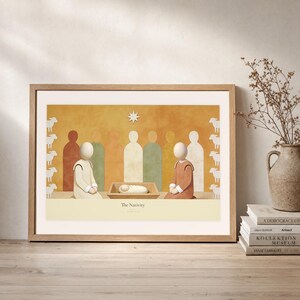 Leaning frame mockup of The Nativity on a rustic wood console beside stacked art books and a tall ceramic vessel with dried stems. The print shows the wrapped child in a low manger between two kneeling figures, beneath a single star. The oak frame, broad cream mat, plaster wall, and soft side light create a relaxed display while keeping the title and Luke 2:7 legible.