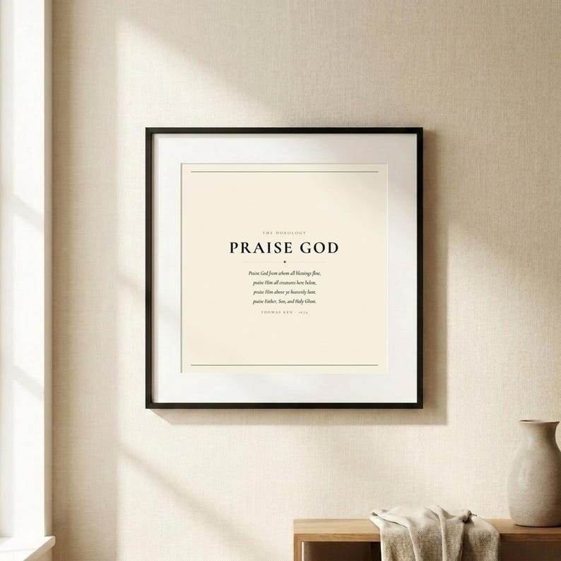 Doxology Praise God From Whom All Blessings Flow christian hymn art print in thin black frame with white mat on warm cream linen wall, soft natural window light and gentle shadow, dark forest green Cormorant Garamond serif typography on cream, minimalist doxology wall art hero product shot baptism wedding