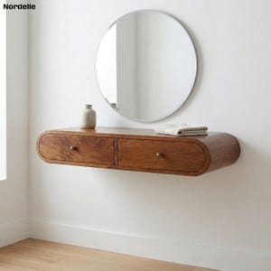 May include: A floating wooden vanity with two drawers and brass knobs. A round mirror hangs above the vanity. A small vase and folded towel are on the vanity's surface. The vanity is a warm brown color.