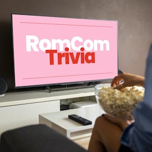 Pode incluir: Um ecrã de televisão mostra as palavras "RomCom Trivia" em branco e vermelho sobre um fundo rosa. Uma pessoa segura uma tigela de pipocas. Um controlo remoto está numa mesa branca.