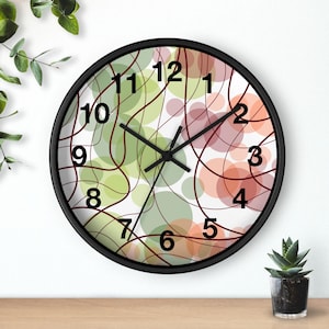 May include: A round wall clock with a black frame and a white face featuring a pattern of overlapping translucent green and peach circles intersected by thin, dark brown curved lines. The clock has black hour, minute, and second hands.