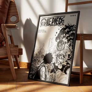 May include: Black framed poster featuring the "ONE PIECE" logo and manga artwork. The poster has a black and white illustration of a character with detailed shading and Japanese text. The poster is leaning against a wall near a wooden chair and shelf.